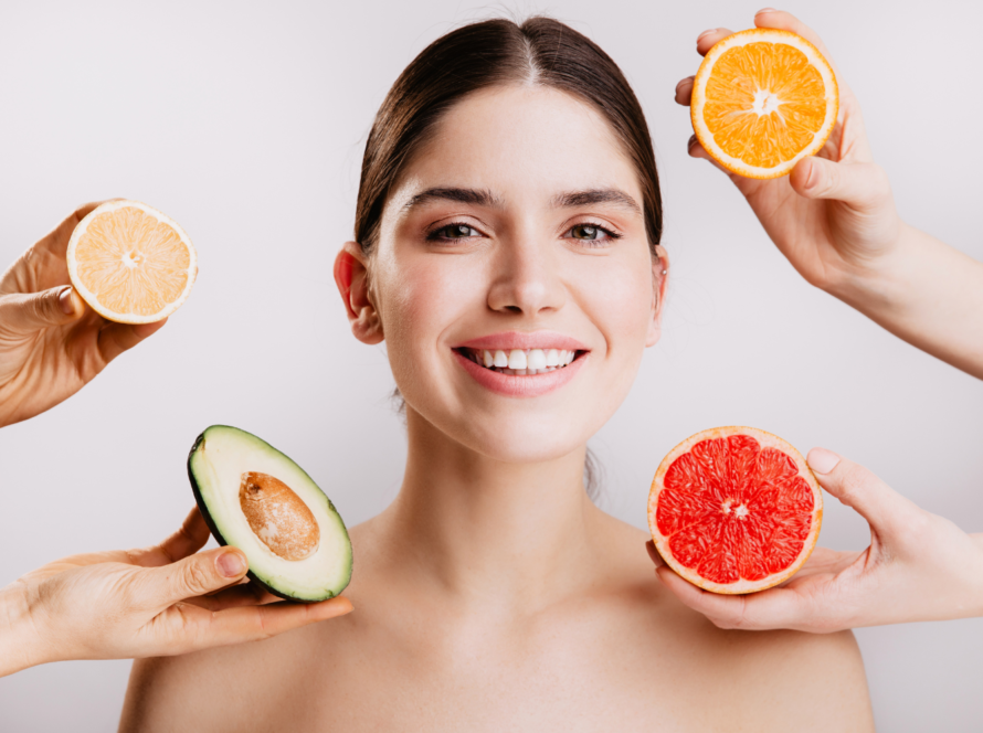 Woman smiling with citrus and avocado near her face.
