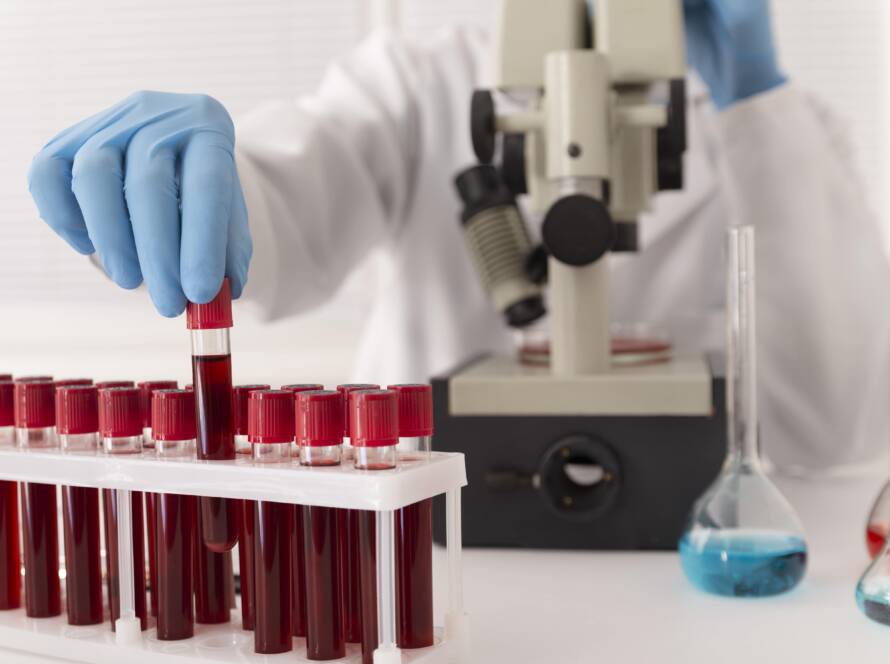 Lab technician prepares blood vials near microscope