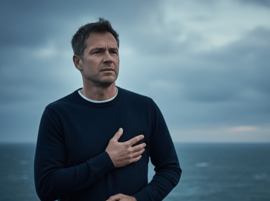 Man holds chest while standing near stormy sea